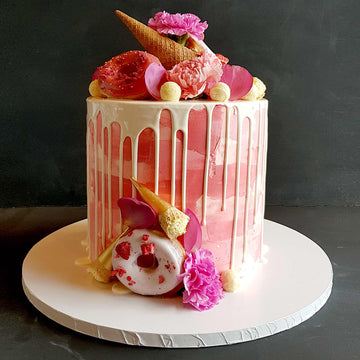Pink buttercream cake with white chocolate drip, donuts and waffle cones