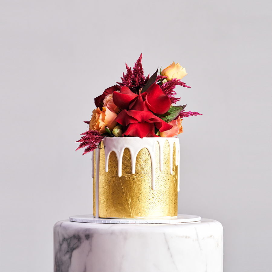 Elegant 23ct gold cake with white drip and vibrant fresh florals